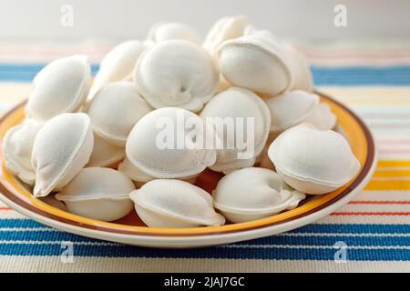 Rohe Knödel auf einem Teller. Gefrorene Knödel mit Fleisch. Halbfertigprodukte aus der Nahaufnahme von Teig und Fleisch. Stockfoto