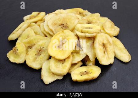 Haufen getrockneter Bananen auf schwarzem Hintergrund. Süße Snacks getrocknete Bananenscheiben. Bio getrocknete Bananenchips aus nächster Nähe. Stockfoto