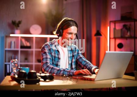 Fokussierter männlicher Manager im Headset, der die Arbeitsbesprechung durch Videoanruf auf dem Laptop leitet. Junger Mann, der redet und gesturiert, während er am Tisch in der Inneneinrichtung sitzt Stockfoto