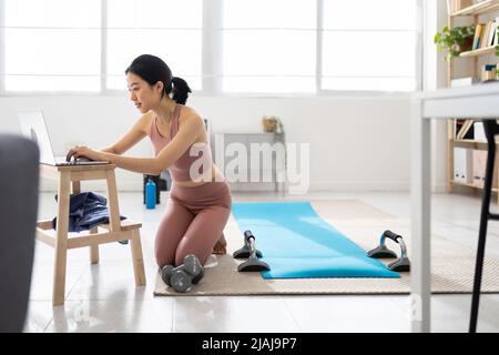 Junge asiatische Frau auf der Suche nach virtuellen Fitness-Klasse auf Laptop zu Hause Stockfoto