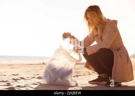 Eine Freiwillige sitzt am Strand und hilft dabei, Meeresmüll aus Plastik zu reinigen. Flaschen zum Beutel nehmen. Ökologisches Recycling Stockfoto