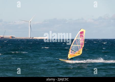 Ein Windsurfer segelt in Pozo Izquierdo, der Stadt der Insel Gran Canaria mit einer Windturbine im Hintergrund. Wassersport-Konzept Stockfoto