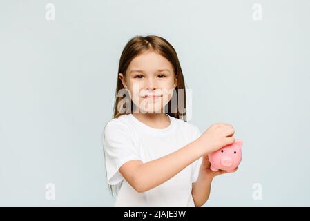 Ein kleines Mädchen steckt eine Münze in ein Sparschwein. Das Konzept, Kindern persönliche Finanzen und Sparen beizubringen Stockfoto