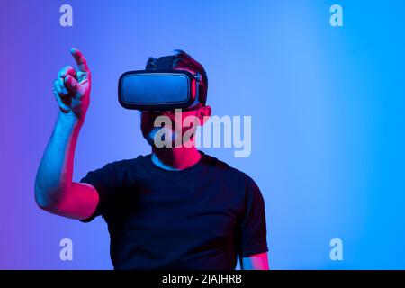 Staunender junger bärtiger Mann, der eine High-Tech-Smart-VR-Brille trägt, 360-Grad-Videos ansieht oder ein Videospiel im Metaverse spielt. Stockfoto