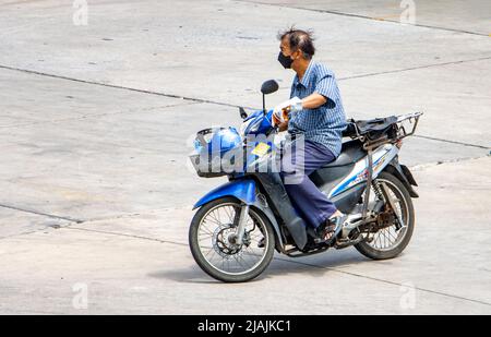 SAMUT PRAKAN, THAILAND, APR 02 2022, Ein Mann mit Gesichtsmaske fährt ein Motorrad Stockfoto