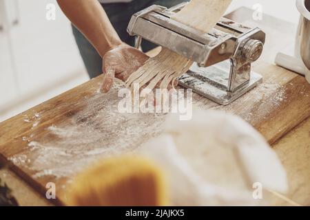 Eine Frauenhand mit Nudel-Slicer-Nudeln auf dem Hintergrund eines Holzbretts aus Mehl Stockfoto