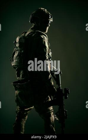 Low-Key-Studioaufnahme des Soldaten der Armee-Spezialeinheiten in taktischem Helm und Kampfuniform, der über die Schulter zurückblickt. Stockfoto