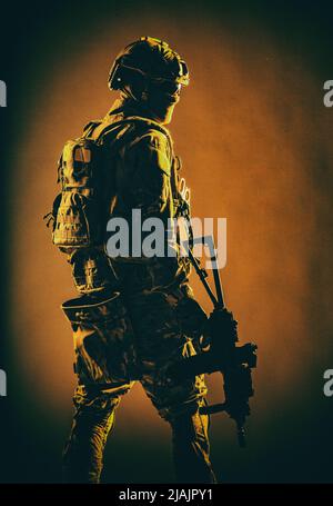 Low-Key-Studioaufnahme des Soldaten der Armee-Spezialeinheiten in taktischem Helm und Kampfuniform, der über die Schulter zurückblickt. Stockfoto