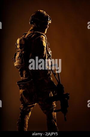 Low-Key-Studioaufnahme des Soldaten der Armee-Spezialeinheiten in taktischem Helm und Kampfuniform, der über die Schulter zurückblickt. Stockfoto