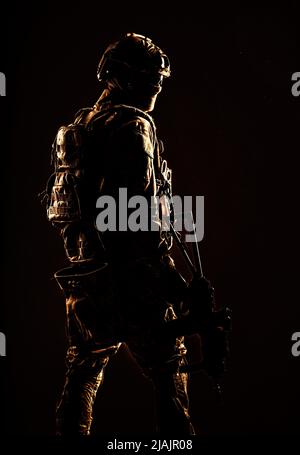 Low-Key-Studioaufnahme des Soldaten der Armee-Spezialeinheiten in taktischem Helm und Kampfuniform, der über die Schulter zurückblickt. Stockfoto