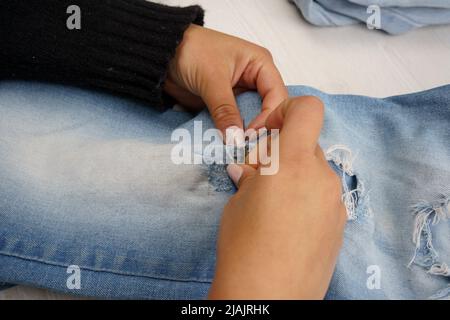 Detail der Hände, die eine Hose mit Nadel und Faden nähen, Näherungsarbeit, Werkzeuge im Studio Stockfoto