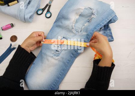 Messen einer jean mit einem Maßband, Arbeitsdetails der Hände, Lifestyle und Nähwerkzeuge auf dem Arbeitstisch Stockfoto