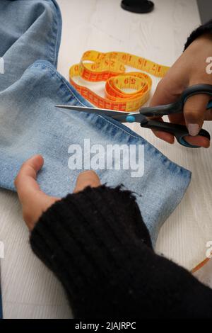 Umgestaltung von Kleidung, Schneiden von jean Stoff mit einer Schere, auf einem Arbeitstisch ein Maßband, Nähinstrumente, Beruf und Tapete Stockfoto