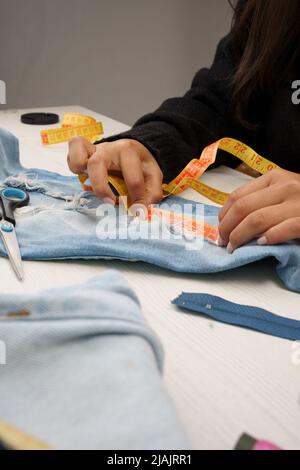 Nähwerkstatt, Messen, um ein Kleidungsstück zu reparieren, verwenden Sie ein Maßband, zusammen mit farbigen Fäden, Instrumente, um im Studio zu arbeiten, Nähen Hobbys Stockfoto