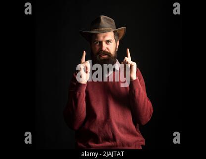 Lustiger Cowboy-Mann mit Cowboy-Hut. Wilde Westwaffen, Fingerrevolver schießen. Cowboy Mann zeigen Finger Pistole. Stockfoto