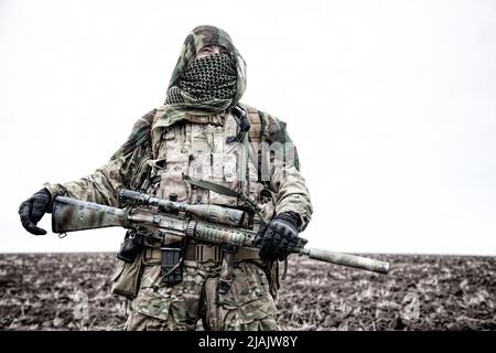 Armeesiper mit Gewehr auf dem Feld, Gesicht hinter shemagh versteckt. Stockfoto