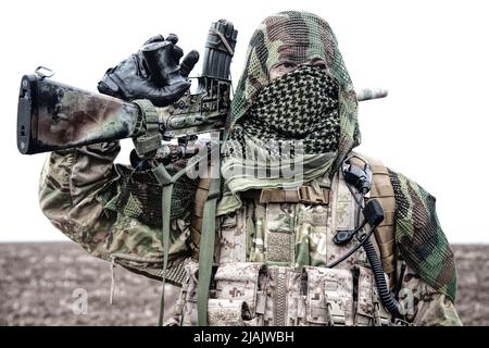 Armeesiper mit Gewehr auf dem Feld, Gesicht hinter shemagh versteckt. Stockfoto