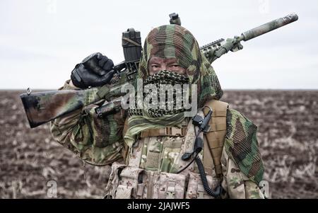 Armeesiper mit Gewehr auf dem Feld, Gesicht hinter shemagh versteckt. Stockfoto