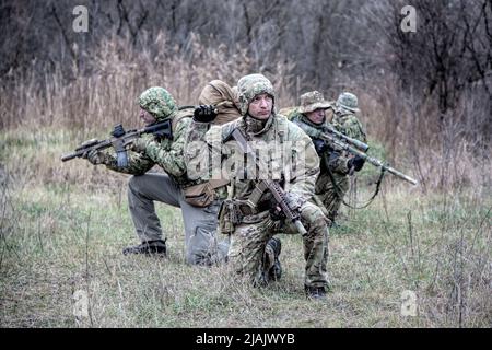 Militärisches taktisches Team bewegt sich vorsichtig in einem Waldgebiet, kniet und schaut sich um. Stockfoto