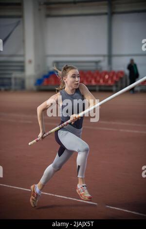 Stangenhochsprungungen im Innenbereich - junge sportliche Frau, die mit einem Stangenstock in den Händen läuft Stockfoto