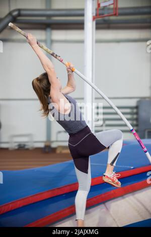 Stangenschwinger im Innenbereich - junge sportliche Frau mit Pferdeschwanz, der sich auf den Stangenpfosten lehnt und im Begriff ist, zu springen Stockfoto