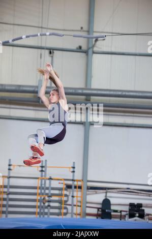 Stangenhochsprung im Haus - junge sportliche Frau mit einem Pferdeschwanz, der nach dem Sprung herunterfällt Stockfoto