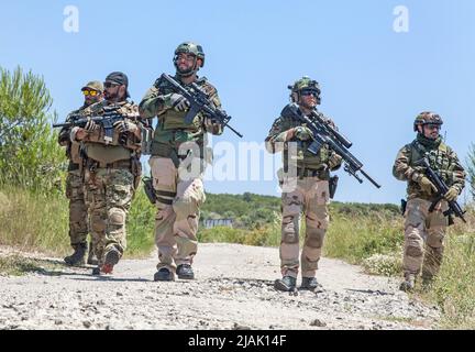 Bewaffnete Soldaten, die zu Fuß auf dem Land patrouillieren Stockfoto