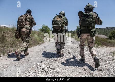 Soldaten, die eine Landstraße entlang laufen, zielen mit ihren Waffen auf Grasflächen. Stockfoto