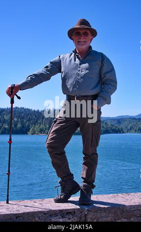 Älterer Mann in Jagdkleidung, der am Seeufer steht Stockfoto