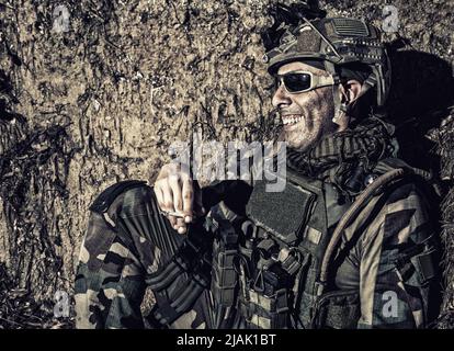 Ein Soldat, der nachts in den Schützengräben ruht und lächelt, während er eine Zigarette raucht. Stockfoto