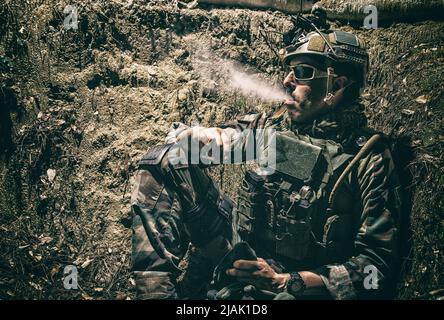 Ein Soldat, der nachts in den Schützengräben ruht und eine Zigarette raucht. Stockfoto