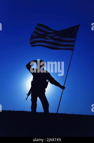 Silhouette eines saluierenden US-Soldaten, der die Nationalflagge gegen den mondbeleuchteten Nachthimmel hält. Stockfoto