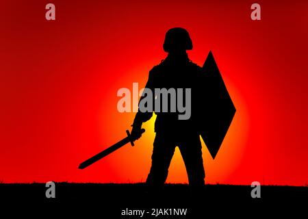 Silhouette eines Soldaten mit Schwert und Schild bewaffnet, mit Sonnenuntergang im Hintergrund. Stockfoto