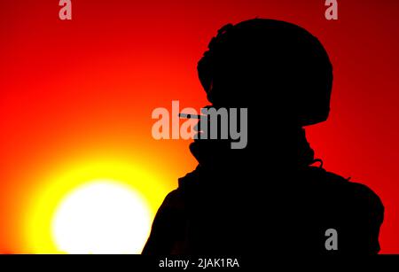 Silhouette eines Soldaten, der nachts vor einem roten Sonnenuntergang Zigarette raucht. Stockfoto