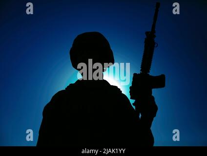 Silhouette eines Soldaten, der mit Gewehr in den Händen gegen einen mondbeleuchteten Nachthimmel steht. Stockfoto