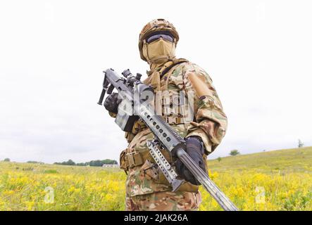Bewaffneter Soldat der Spezialeinheiten mit Scharfschützengewehr, das im Feld steht. Stockfoto