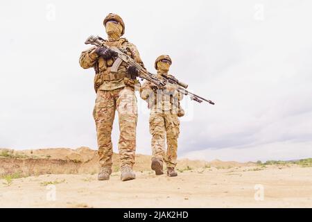 Bewaffnete und bewaffnete Soldaten der Spezialeinheiten mit Gewehren während der Militäraperation in der Wüste. Stockfoto