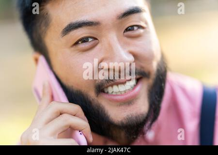 Nahaufnahme eines chinesischen Mannes, der mit dem Handy lächelt. Stockfoto
