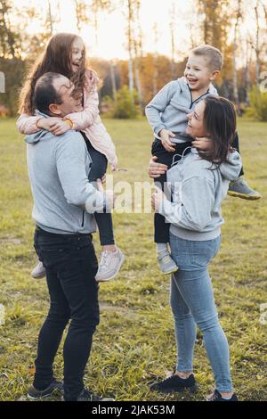 Die Familie verbringt den Nachmittag zusammen, Eltern tragen Kinder in den Armen, während sie durch den Park gehen. Viel Spaß mit der Familie. Ein schönes Wochenende Stockfoto