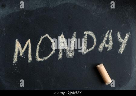 Montag. Name des Wochentags, der in gelber Kreide auf einer schwarzen Tafel geschrieben ist. Handgeschriebener Text. Daneben liegt ein Stück farbige Kreide. Stockfoto