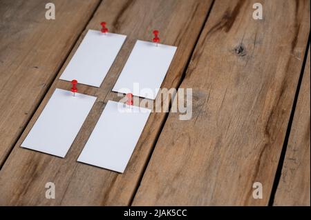 Leere Visitenkarten vor einem hölzernen Hintergrund. Vier Rechtecke aus weißem Papier, die mit Stecknadeln an alten Brettern befestigt sind. Selektiver Fokus. Stockfoto