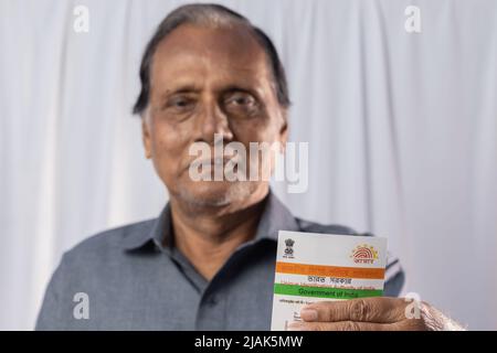 Birbhum, Westbengalen / Indien - 15. März 2022: Selektiver Fokus auf die Aadhaar-Karte, die von einem alten indischen Mann mit lächelndem Gesicht in der Hand gehalten wird Stockfoto