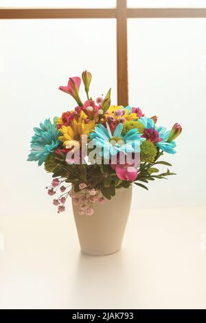 Ein kleiner Strauß gelber und blauer Chrysanthemen auf einem weißen Tisch in der Nähe des Fensters. Vertikale Aufnahme. Stockfoto