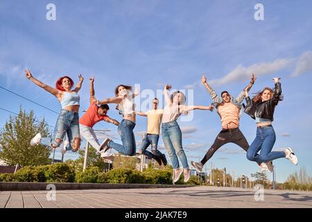 Eine Gruppe glücklicher Freunde lächelt der Kamera zu, während sie im Freien zusammen springen. Freundschaft und Glück Konzept. Stockfoto