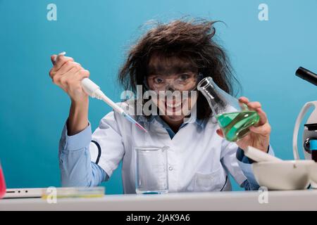 Grinsend gruselig verrückt verrückt Wissenschaftler mit Tropfer und Becher mischen experimentelle flüssige chemische Substanzen. Verrückter Chemiker mit furchtbarer Gesichtsausdruck, der Laborarbeit leistet. Stockfoto