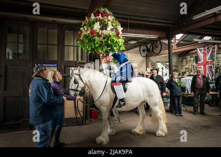 Der zeremonielle König, Jon Haddock, wird während der Castleton Garland in eine große Girlande verholfen, eine alte Tradition, bei der der König einen großen, mit Blumen bedeckten Rahmen anzieht, bevor er eine Prozession zu Pferd durch das Dorf Castleton im Peak District National Park in Derbyshire führt. Bilddatum: Montag, 30. Mai 2022. Stockfoto