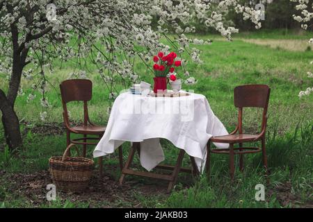 Steel Life - Frühstück im Frühlingsgarten. Tisch mit weißer Tischdecke zum Teetrinken serviert Stockfoto
