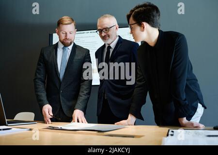 Geschäftspartner in formellem Anzug, der sich den Bericht am Tisch ansieht und die Arbeit im Team im Büro plant Stockfoto
