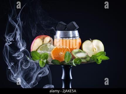 Obstschale für Shisha mit Orange, Apfel, Limette, Mandarine, Minze mit Kaluda, Mit Kokoskohle und Rauch auf schwarzem Hintergrund Stockfoto