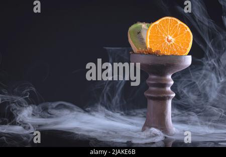 Obstschale mit Tabak, Kiwi, Mandarine und Rauch auf schwarzem Hintergrund Stockfoto